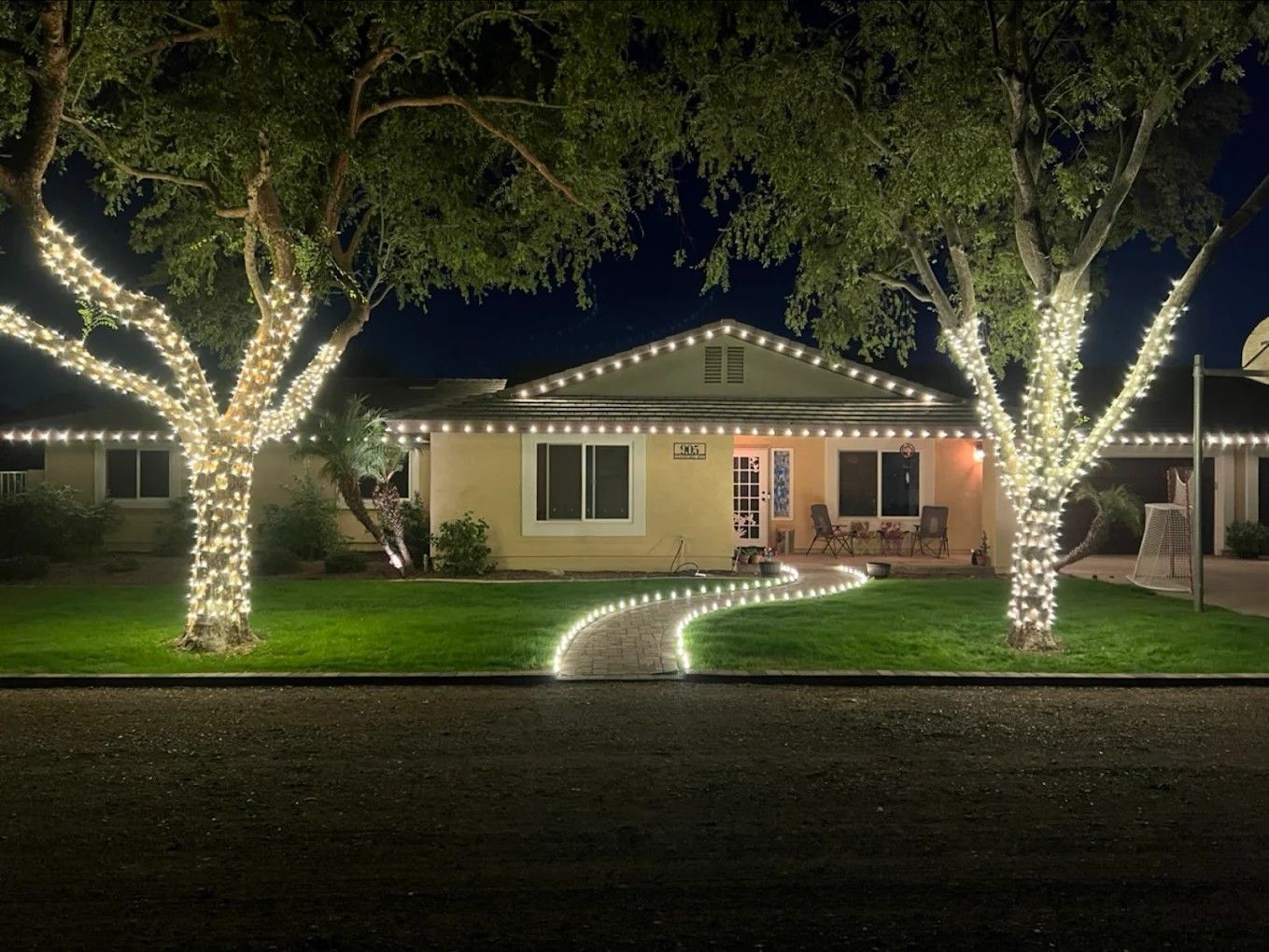 House lit with white lights, glowing trees, and a curved lighted walkway at night