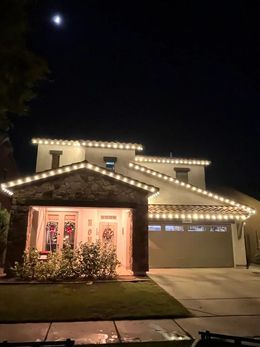 Single-story house at night with warm white holiday lights outlining the roof and porch.