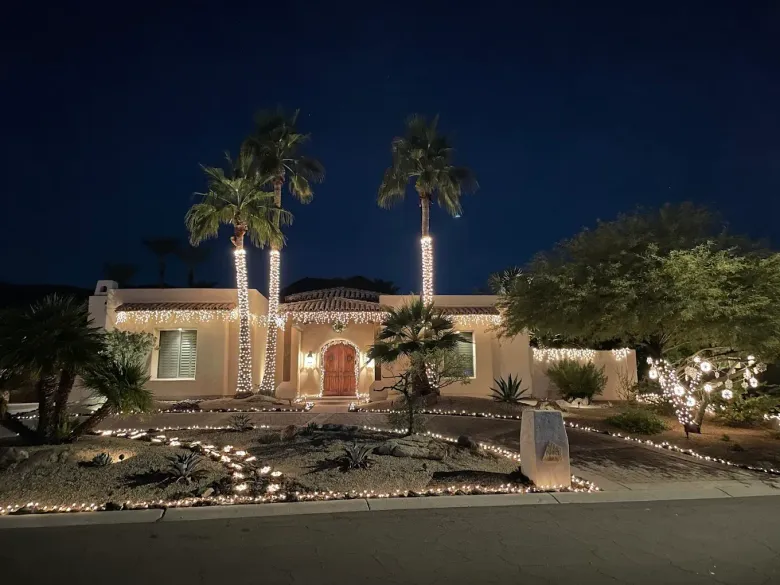 Night view of a lit stucco house with palm trees and a landscaped front yard