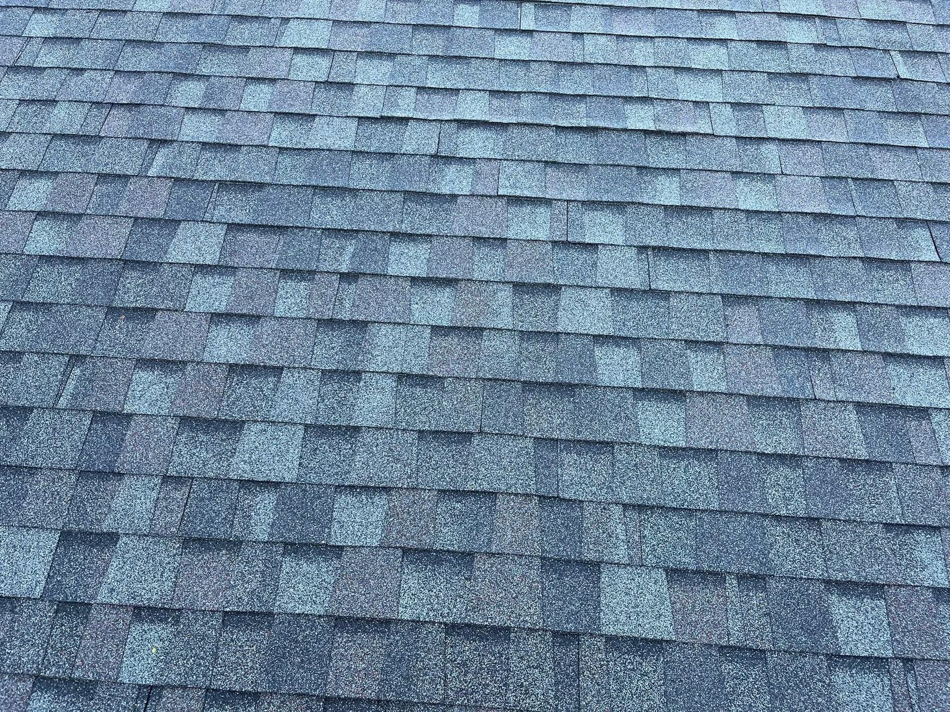 A close-up of dark grey, textured asphalt shingles covering a sloped residential roof.