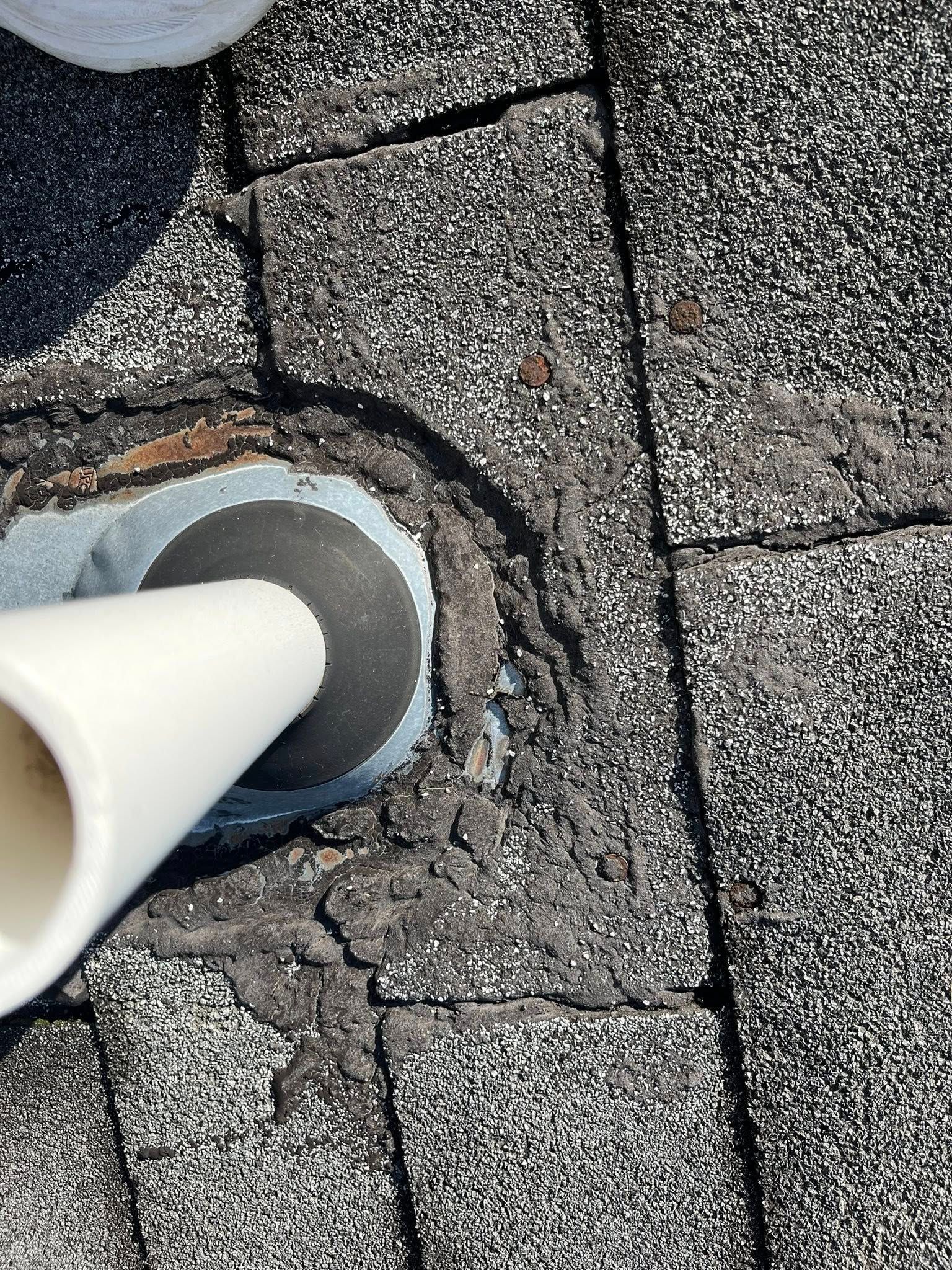 A white plumbing vent pipe emerging from a shingled roof, surrounded by thick, weathered sealant on the metal flashing.