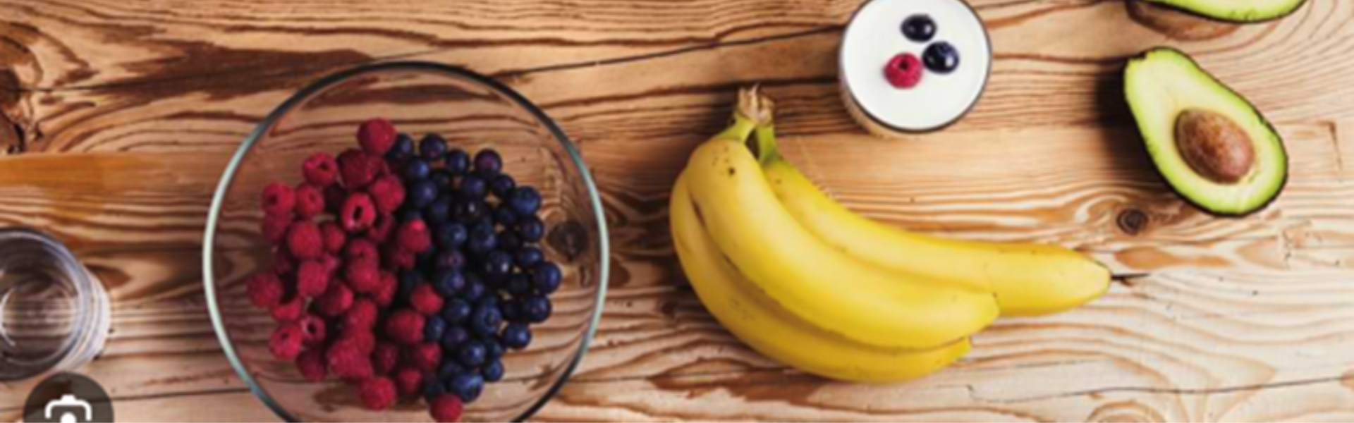 Bowls of berries, bananas, yogurt, and avocado on a rustic wooden table