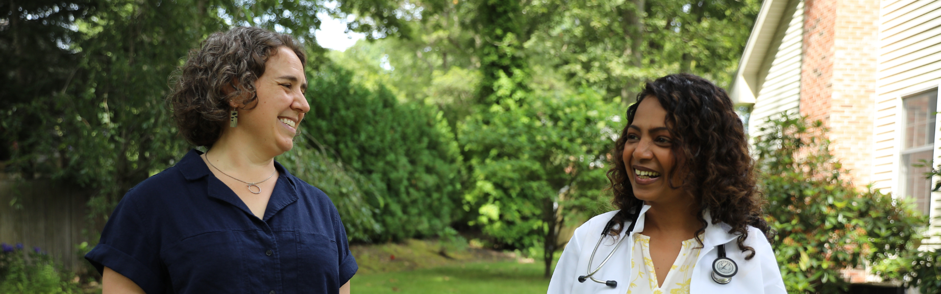 Two people in scrubs smiling outdoors in a green garden setting