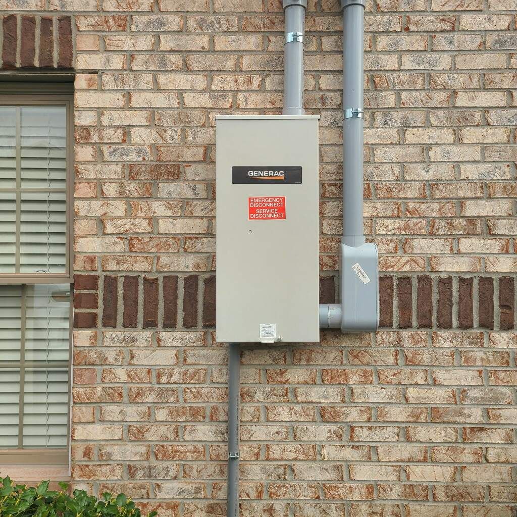 A standby generator mounted on a brick wall with conduits, near a window.