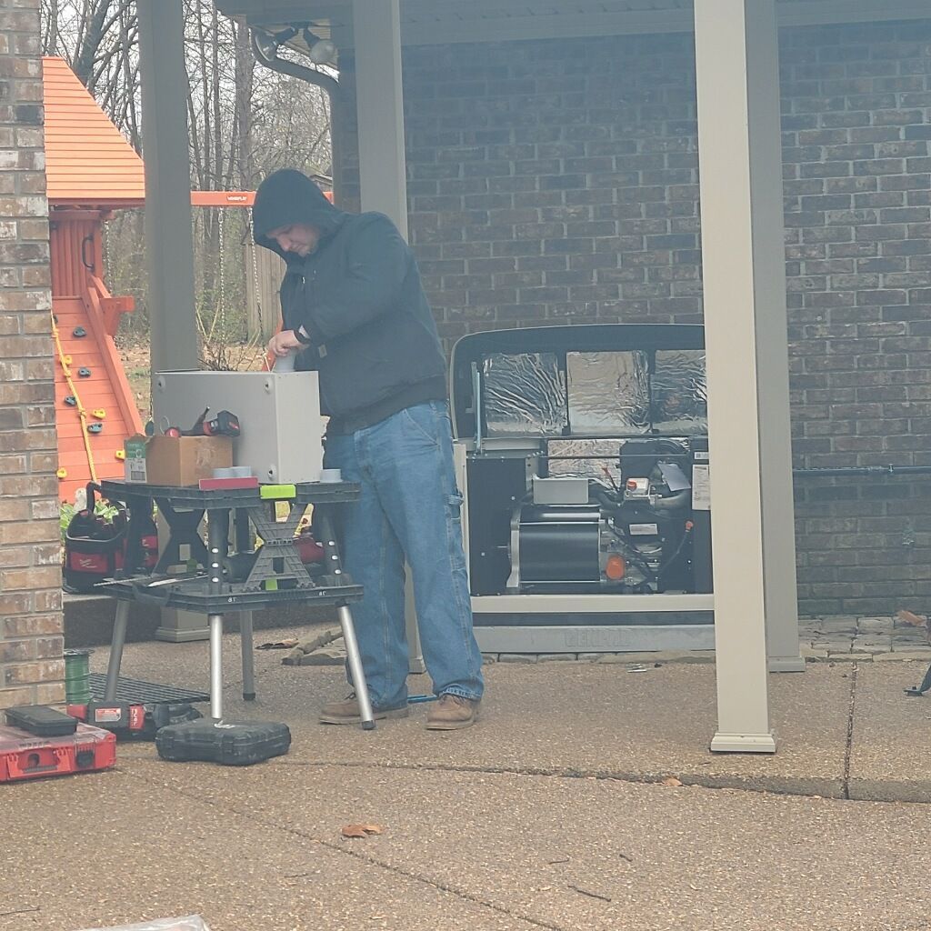 Man in a hooded sweatshirt working on a metal box on a table under a covered patio.