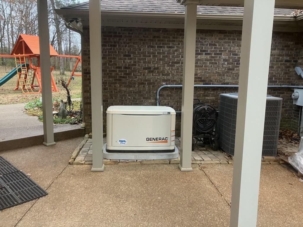 Generator under a covered patio next to an AC unit and brick wall.