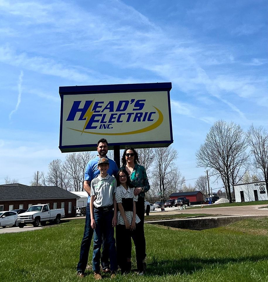 Family poses in front of Head's Electric sign on a sunny day.