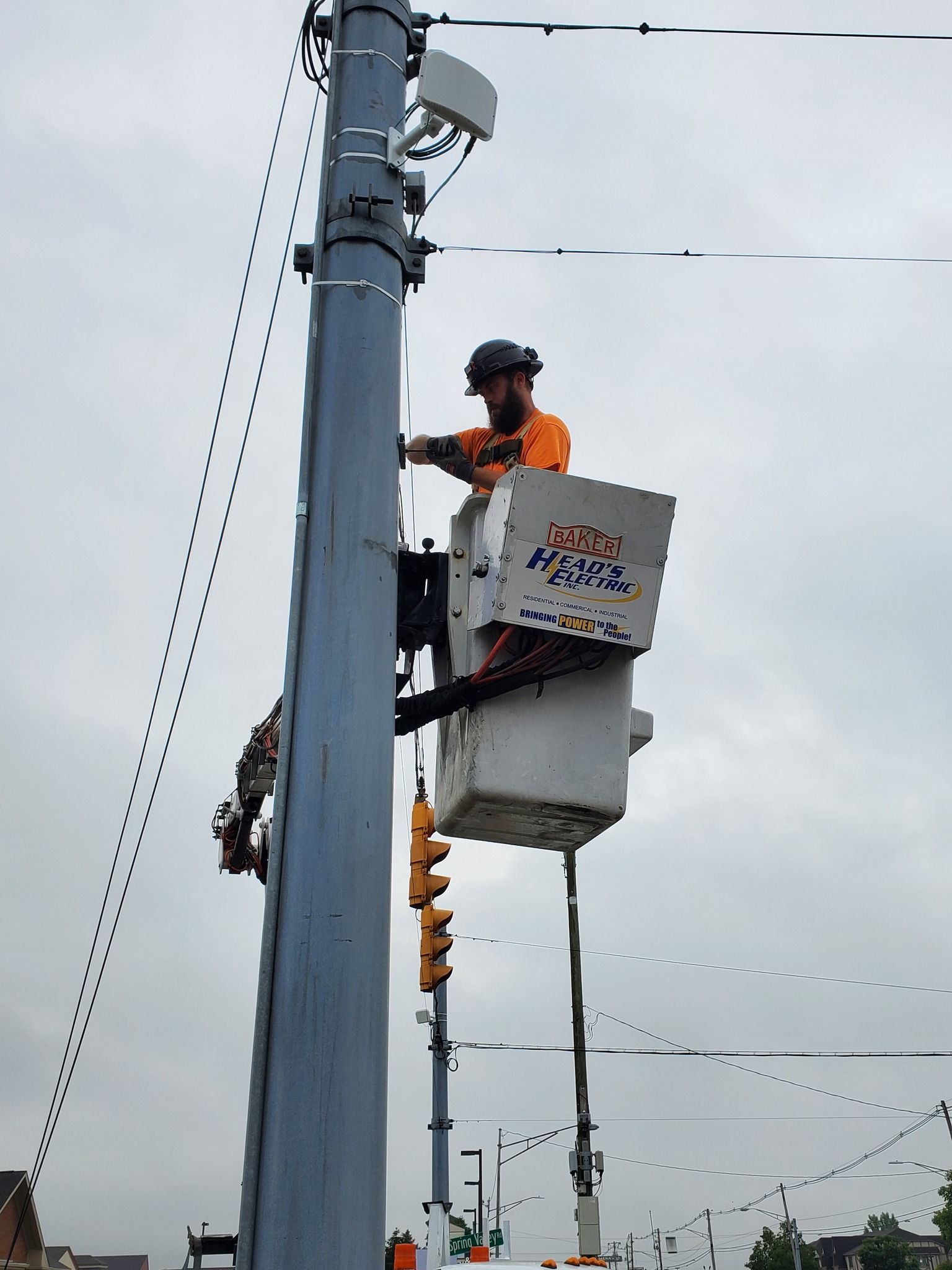 Lineworker in lift bucket working on pole, traffic lights visible. Overcast day.