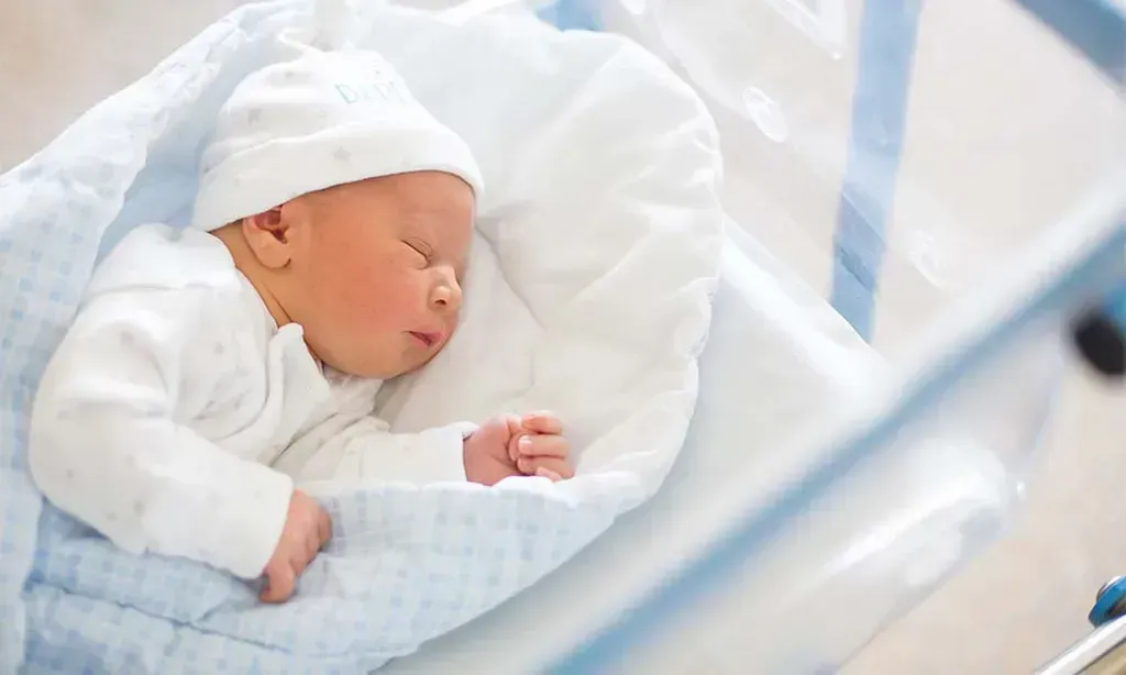 A newborn baby is sleeping in a hospital bed.