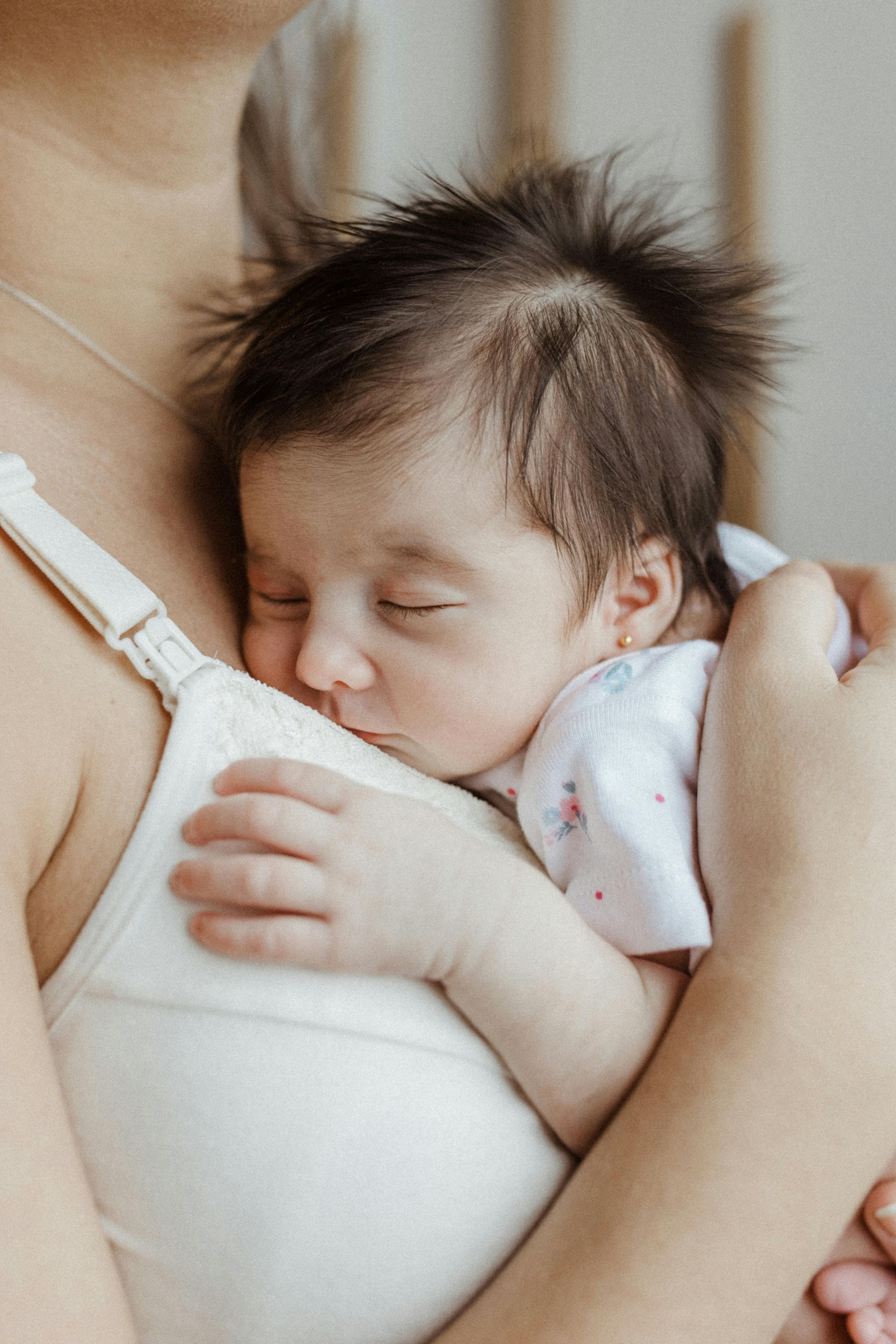 Baby asleep in a person's arms, wearing a white nursing bra.