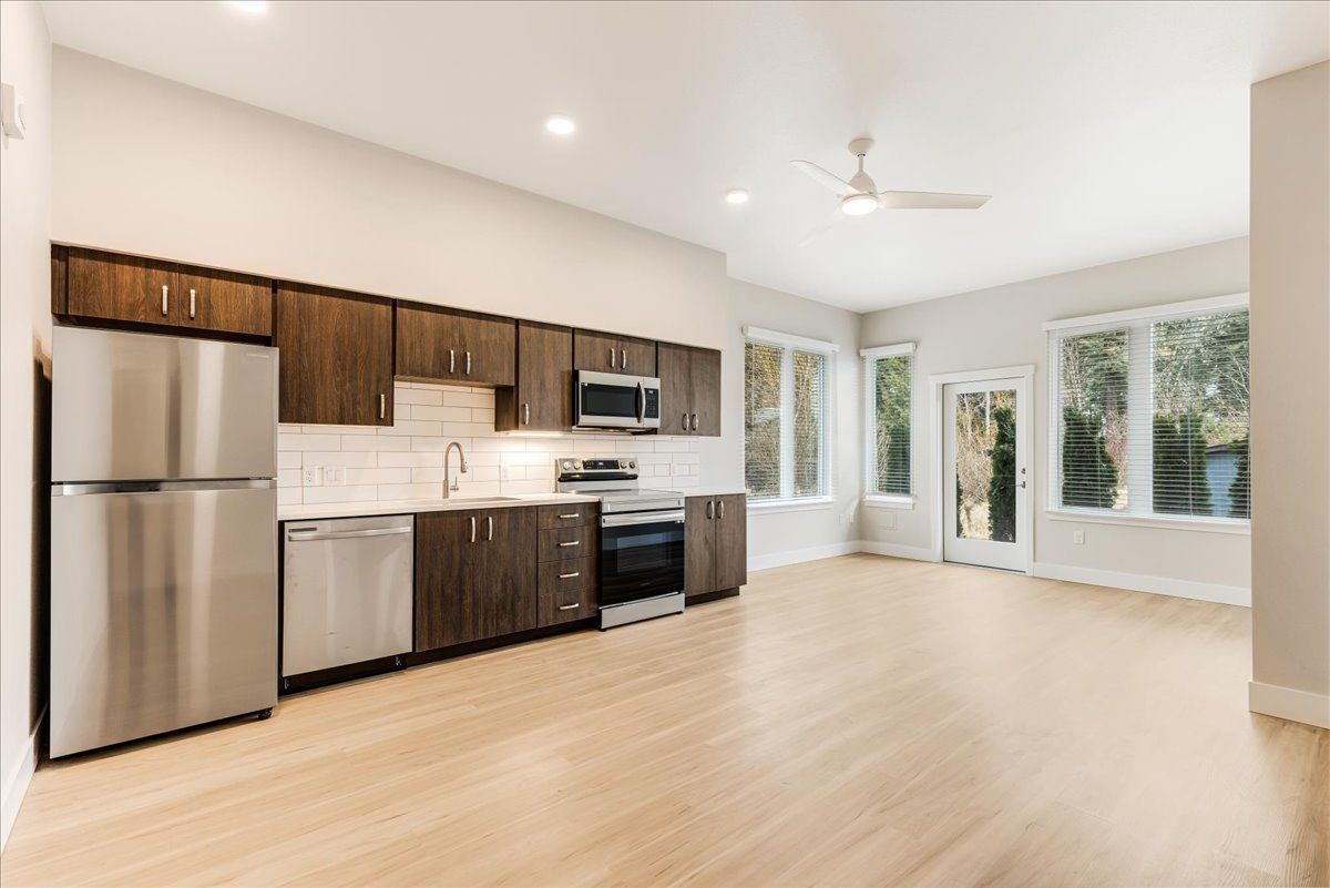 an empty kitchen with stainless steel appliances and wooden floors .