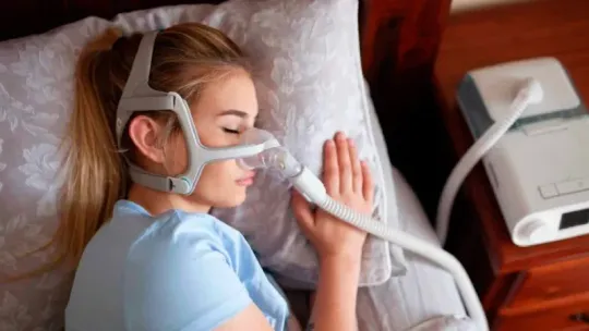Person lying in bed using a breathing mask connected to a medical device