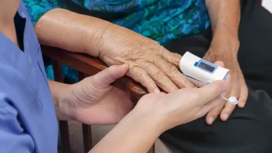 Healthcare worker checking an older patient’s finger with a pulse oximeter in a clinical setting