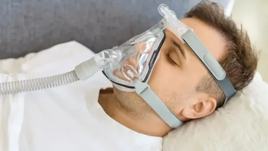Person wearing a CPAP mask sleeping on a bed with a white pillow