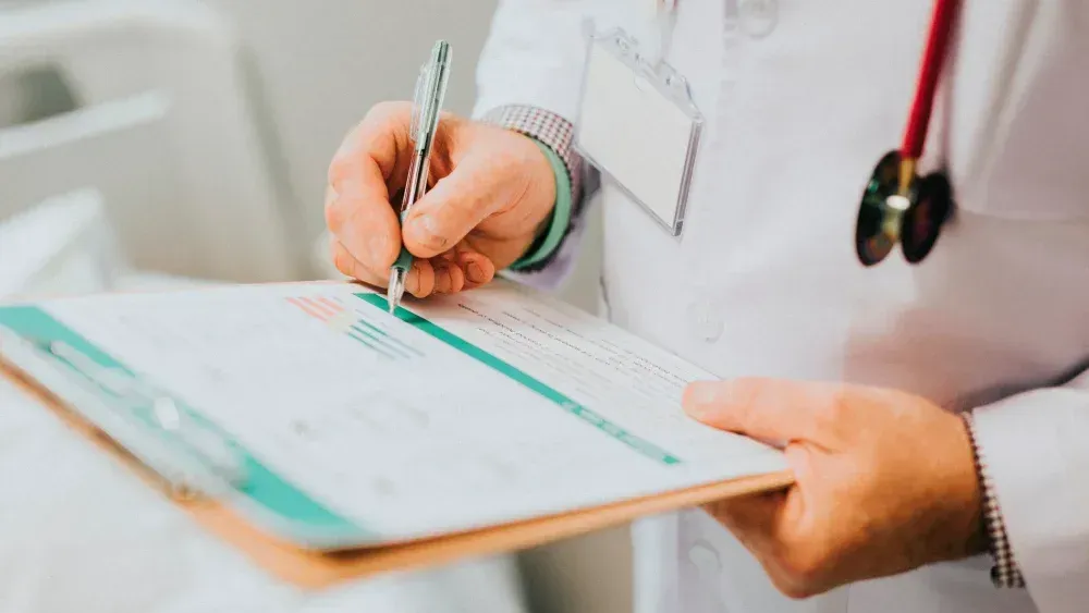Doctor writing on a clipboard in a white coat with a stethoscope around the neck