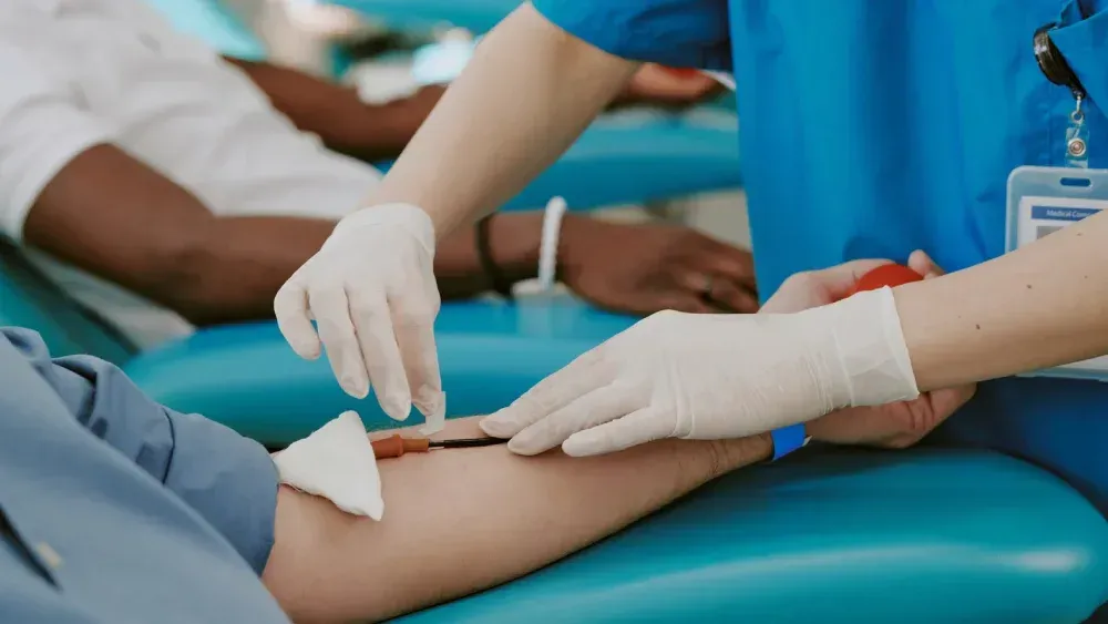 Gloved clinician taking a blood sample from a patient’s arm in a medical clinic