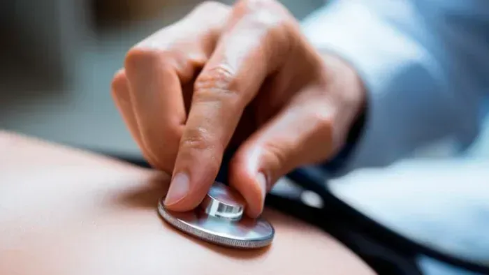 Hand holding a stethoscope to a patient’s skin during a medical checkup