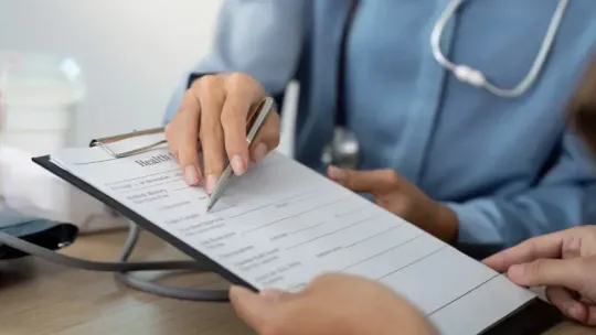 Doctor reviewing a patient form on a clipboard with another person in a clinical setting