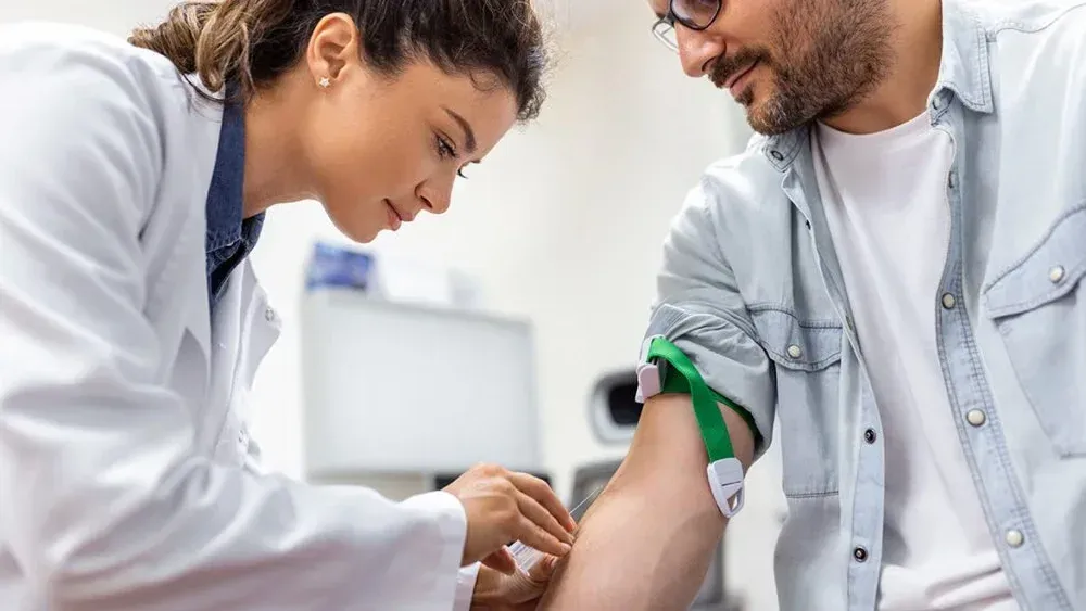 Healthcare worker taking blood from a patient’s arm in a clinic, with both focused on the procedure.