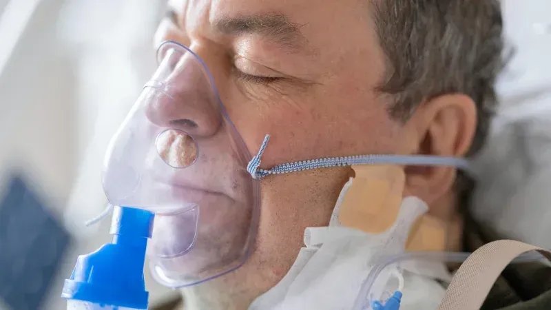 Man receiving oxygen through a nasal cannula and mask, eyes closed in a hospital setting