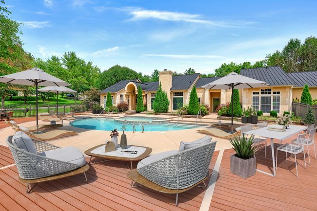 Poolside lounge area with umbrellas, seating, and a building with arched entryways under a blue sky.