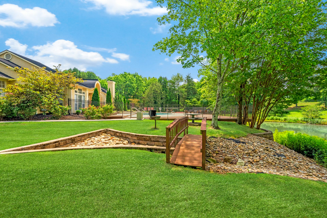 A wooden bridge over a river in a park with a house in the background at Steeplechase Apartments in Knoxville, Tennessee