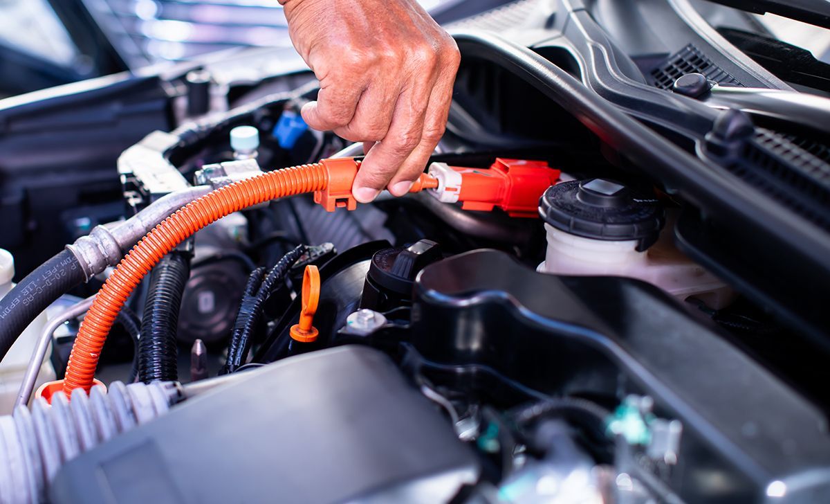 Hand reaching for an orange high voltage cable in a car engine bay.