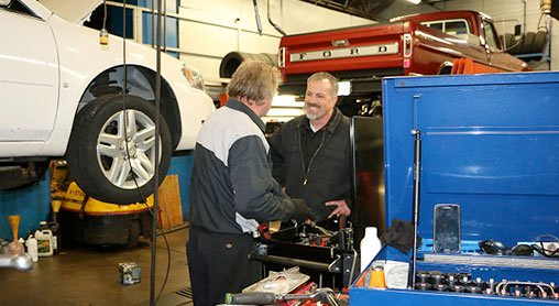Two men are working on a car in a garage.