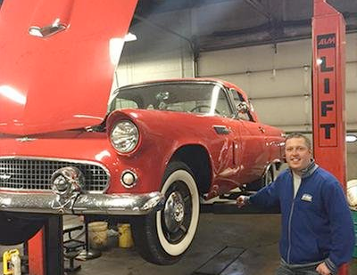 A man is standing next to a red car on a lift.