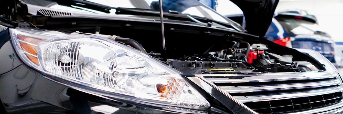 A car with the hood open is being worked on by a mechanic.