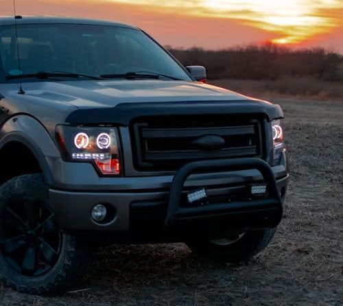 Gray Ford pickup truck with bull bar, custom headlights, parked at sunset.