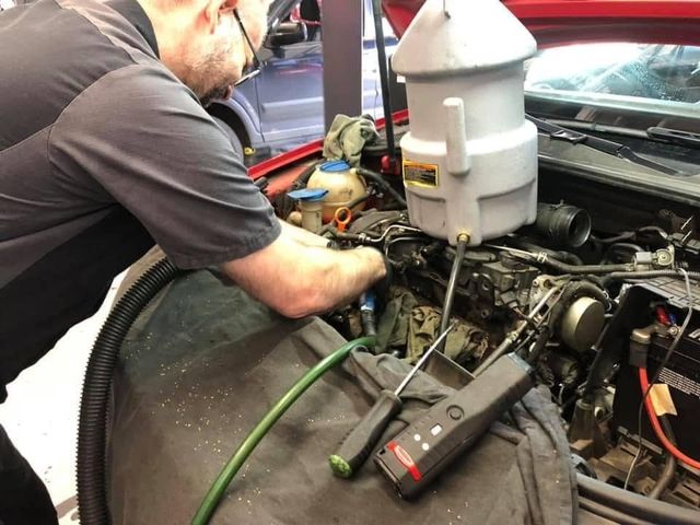 Mechanic working under a car hood with tools and a fluid reservoir in an auto repair shop | Auto Shop NW