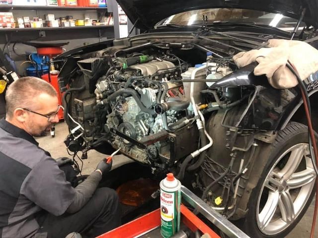 Mechanic inspecting a car engine in a garage, with tools and an open hood. | Auto Shop NW