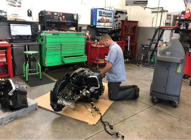 Mechanic kneeling beside an engine in an auto repair shop with green tool cabinets. | Auto Shop NW