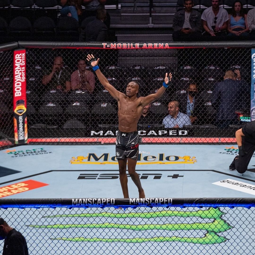 MMA fighter celebrates victory inside the octagon at T-Mobile Arena, arms raised, looking happy.