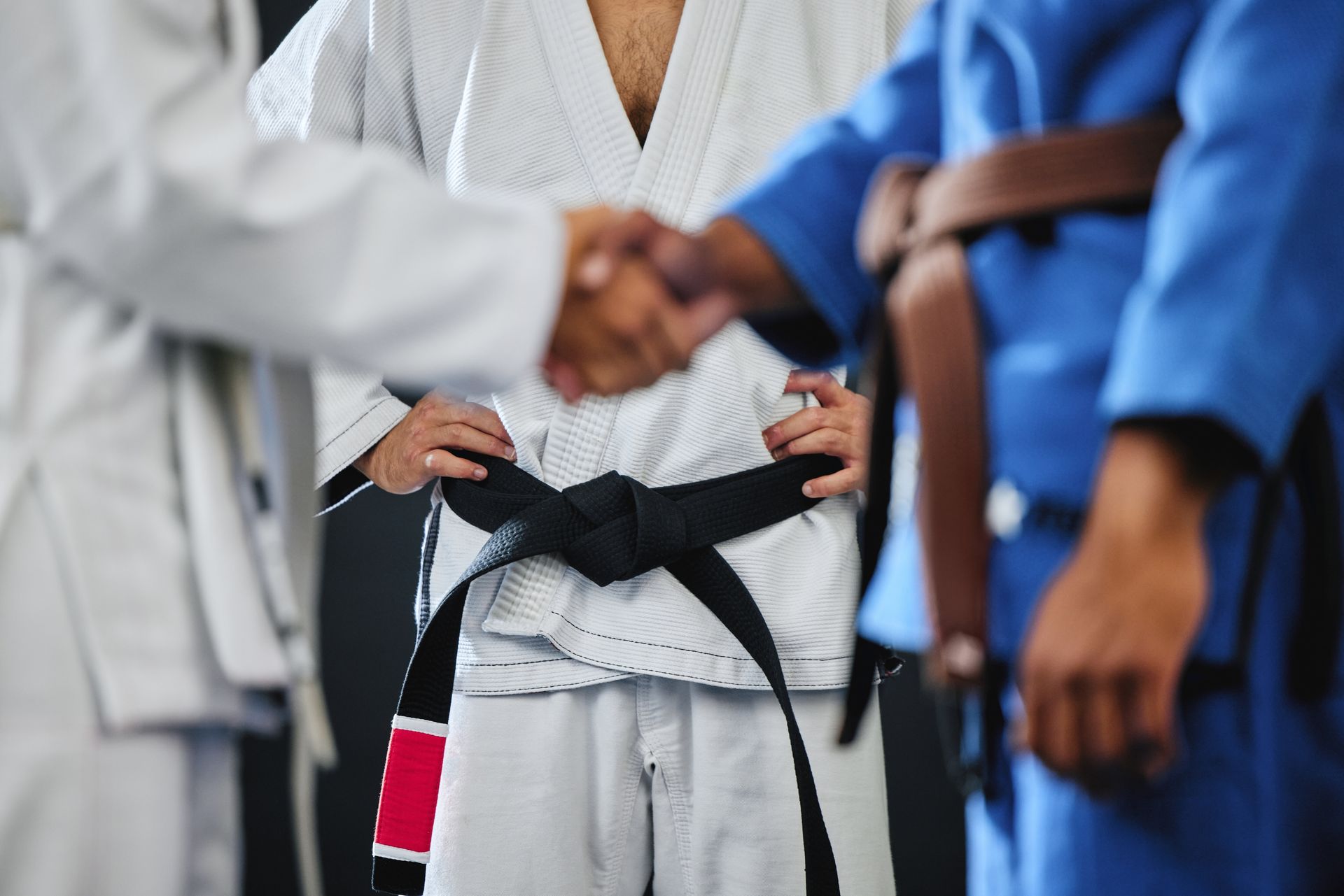 Martial artists in gis shake hands as one ties a black belt at center.