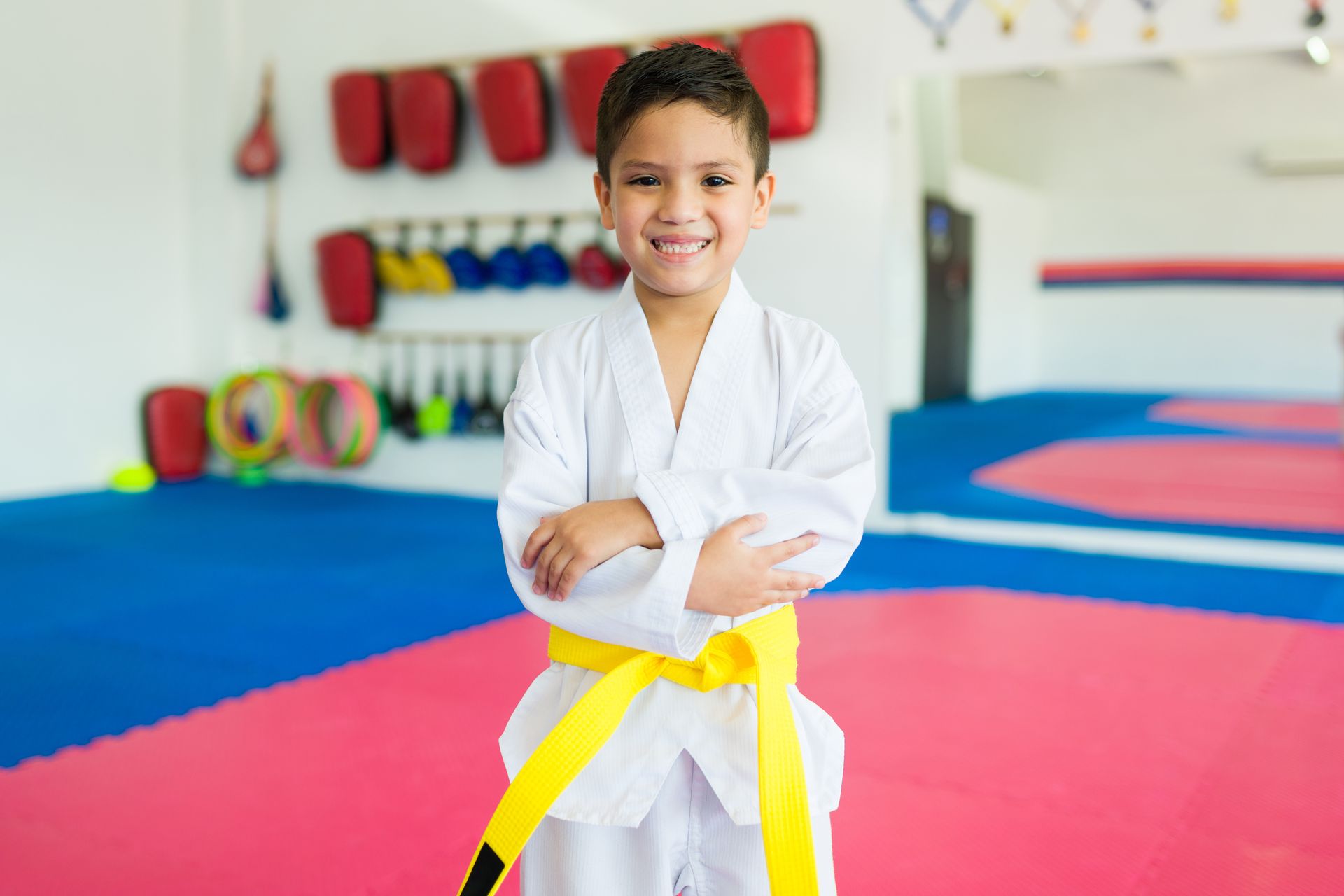 Child in a white martial arts uniform with yellow belt standing in a dojo.