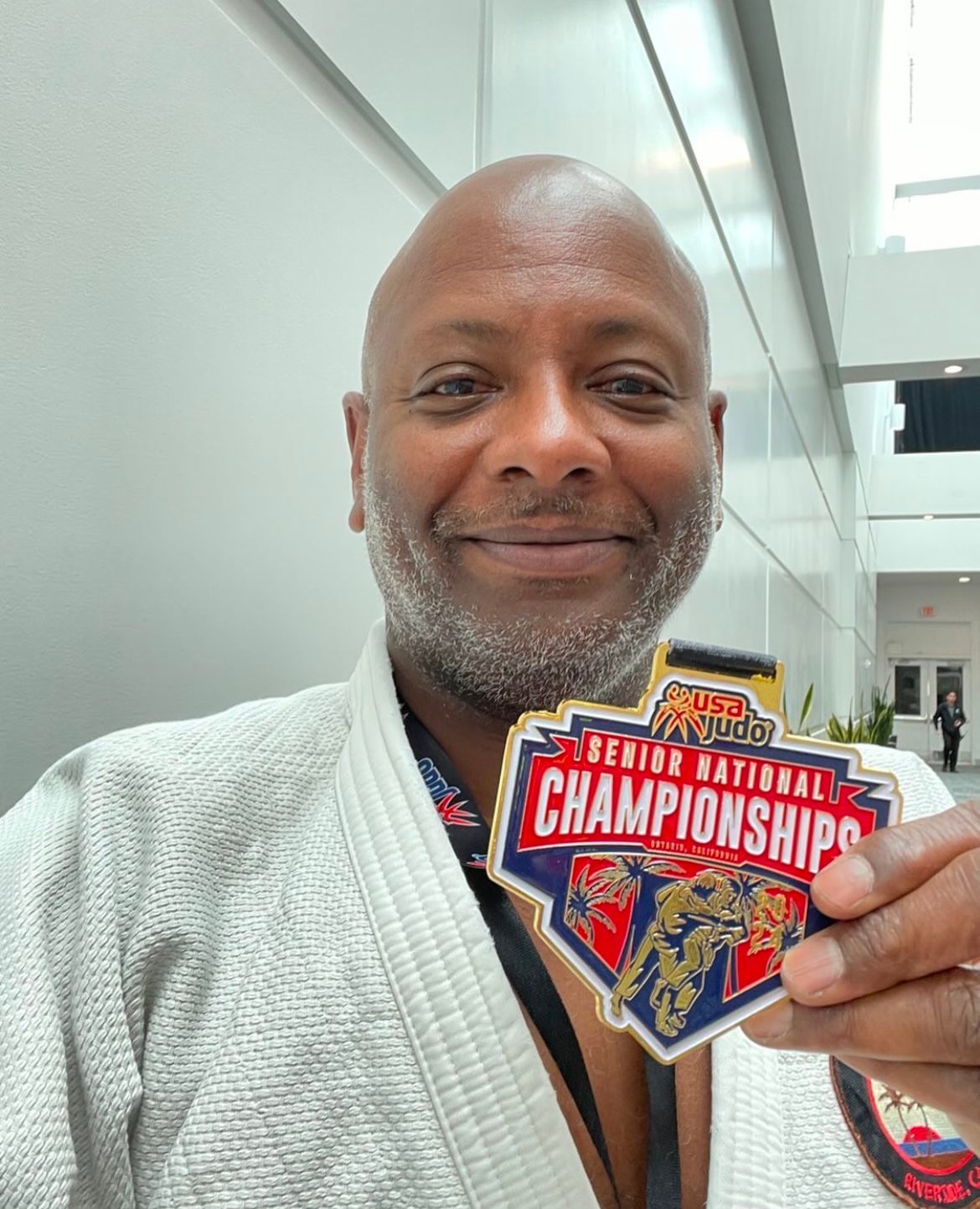 Man in Judo gi smiles, holding Senior National Championship medal.