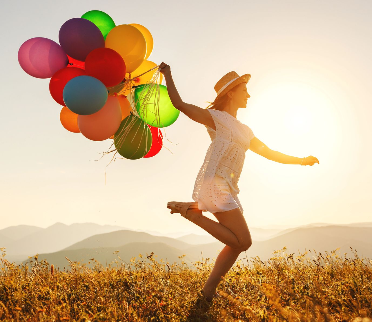 Una persona corre in un campo illuminato dal sole al tramonto, tenendo in mano dei palloncini colorati.