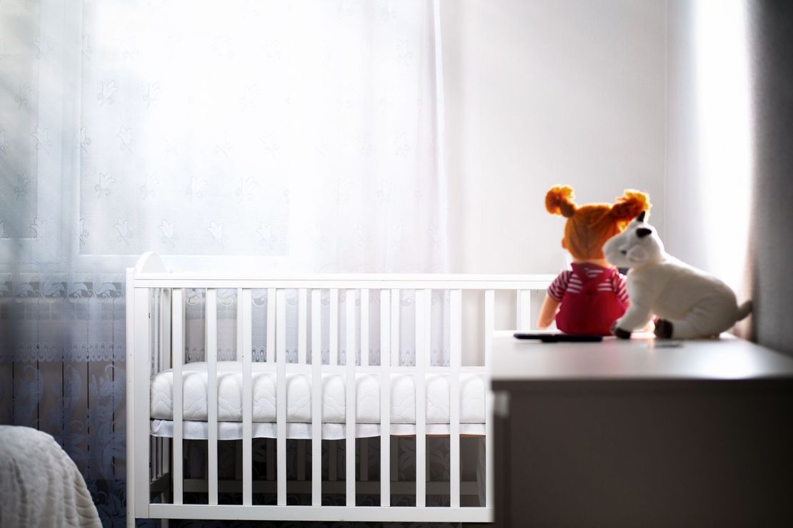 In una cameretta illuminata dal sole, due peluche sono appoggiati su una cassettiera accanto a una culla bianca.