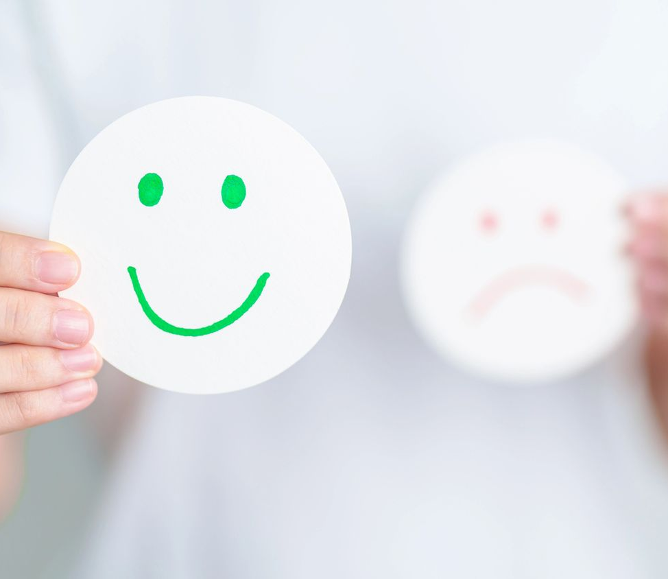 Mani che reggono cartoncini con faccine sorridenti e tristi, con la faccina sorridente verde a fuoco e quella triste sfocata sullo sfondo.