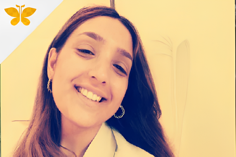 Persona sorridente in interni con un filtro giallo caldo e una piccola icona a forma di farfalla in alto a sinistra.