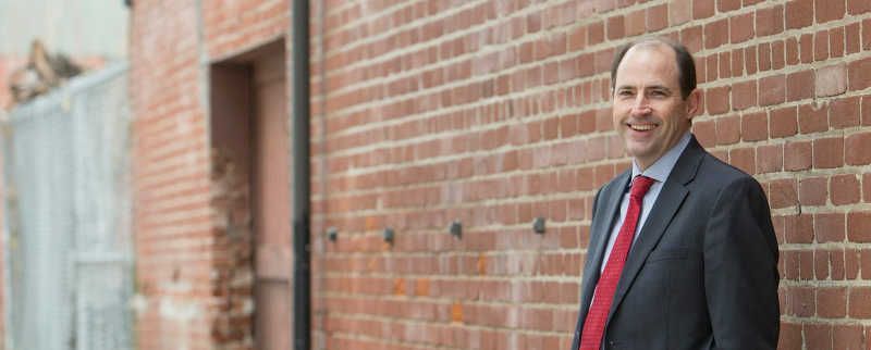 A man in a suit and tie is standing in front of a brick wall.