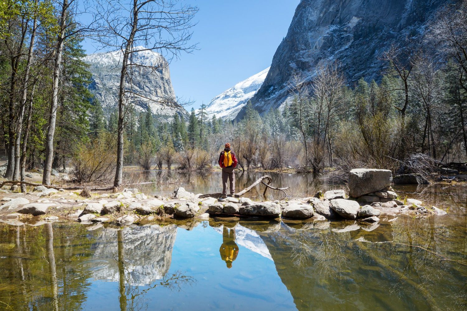 A man with a backpack is standing on a rock overlooking a lake.