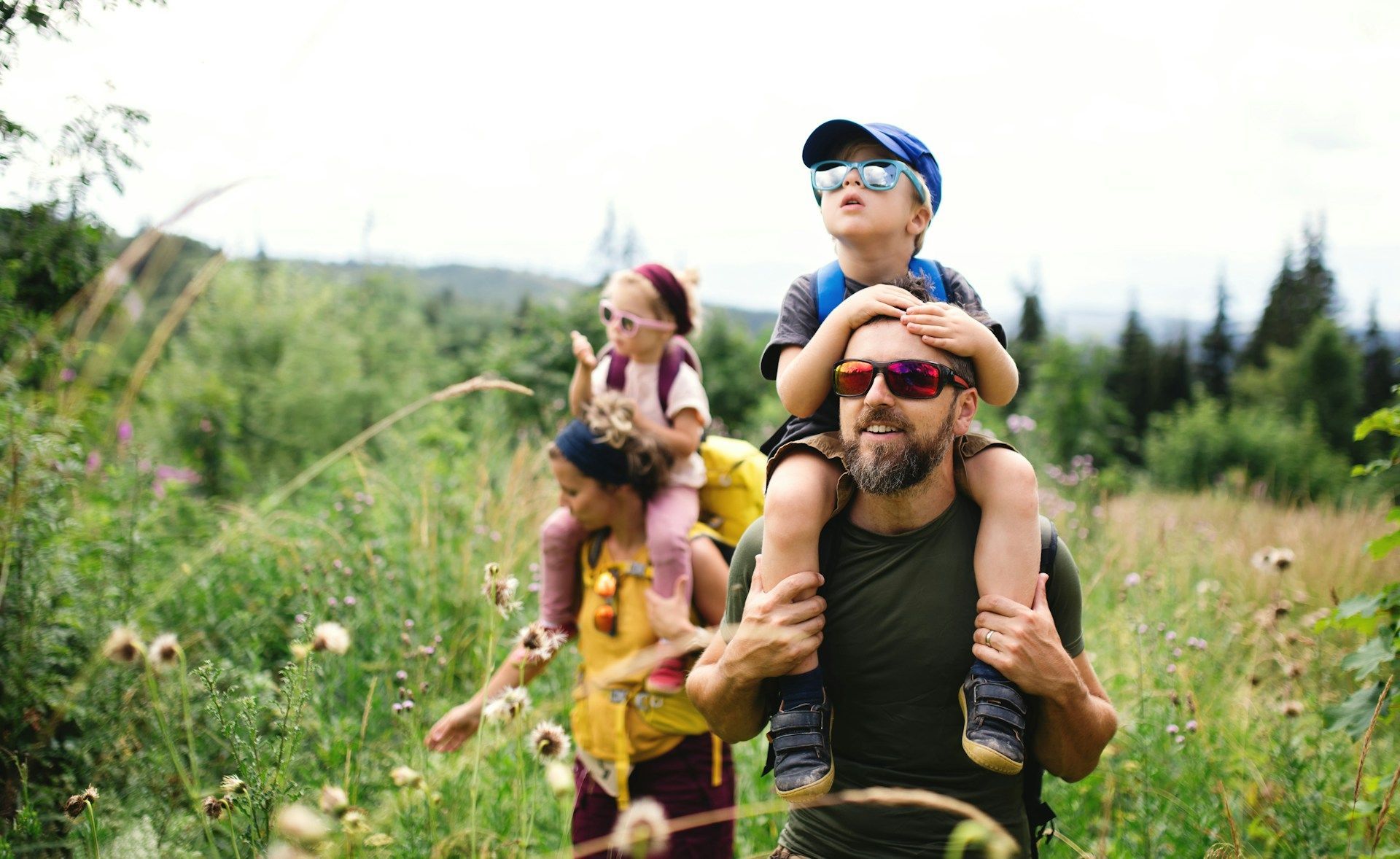 A man is carrying two children on his shoulders while walking through a field.