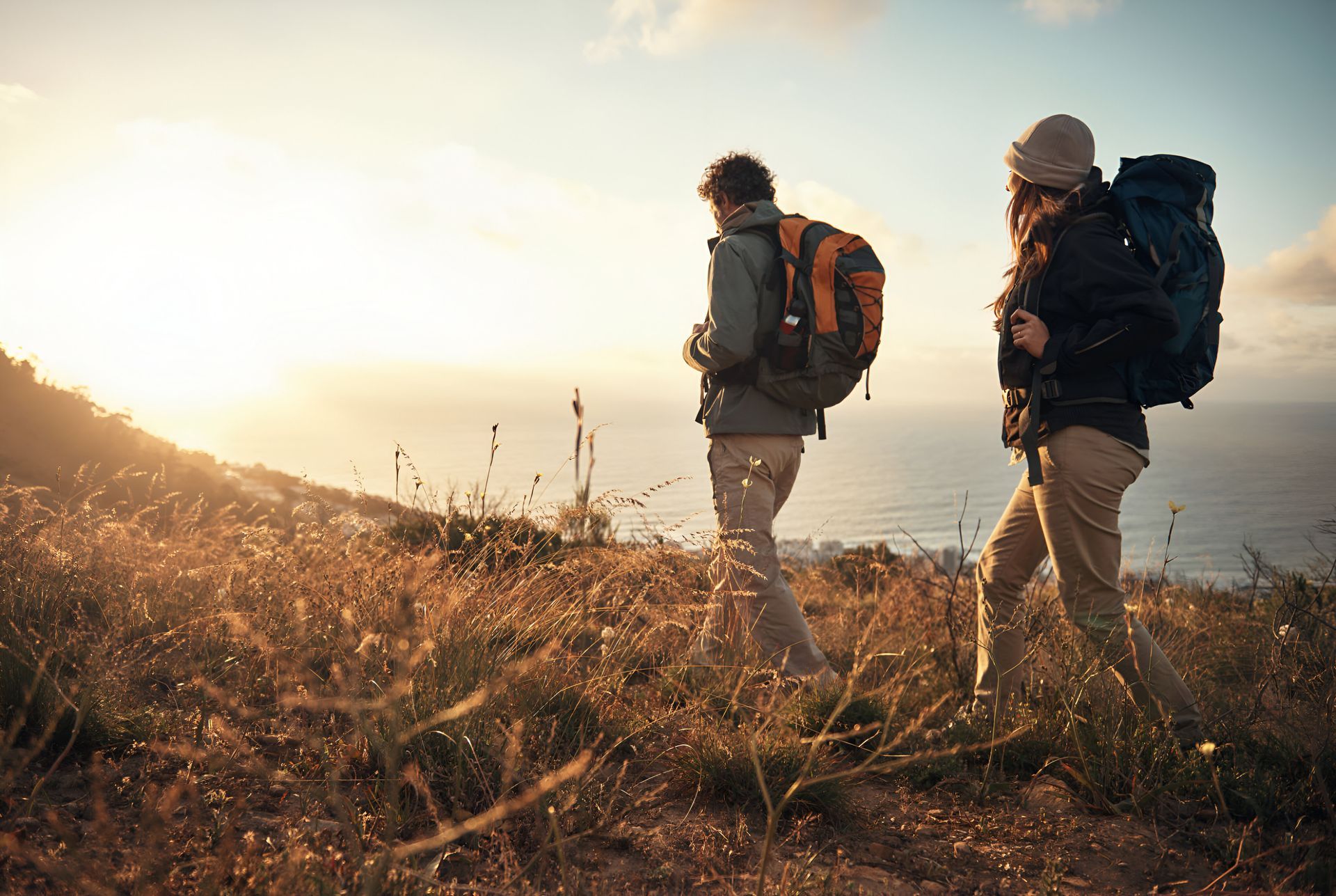 A man and a woman are hiking up a hill with backpacks.