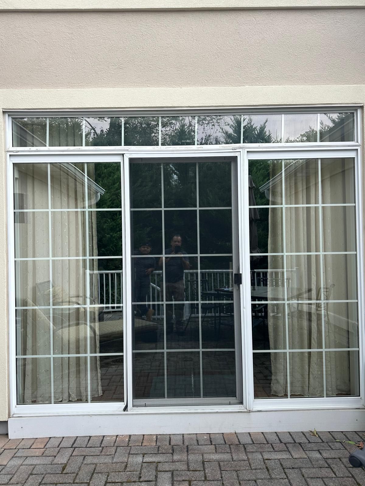 Glass patio doors with curtains and a reflection of outdoor trees, framed by white trim.