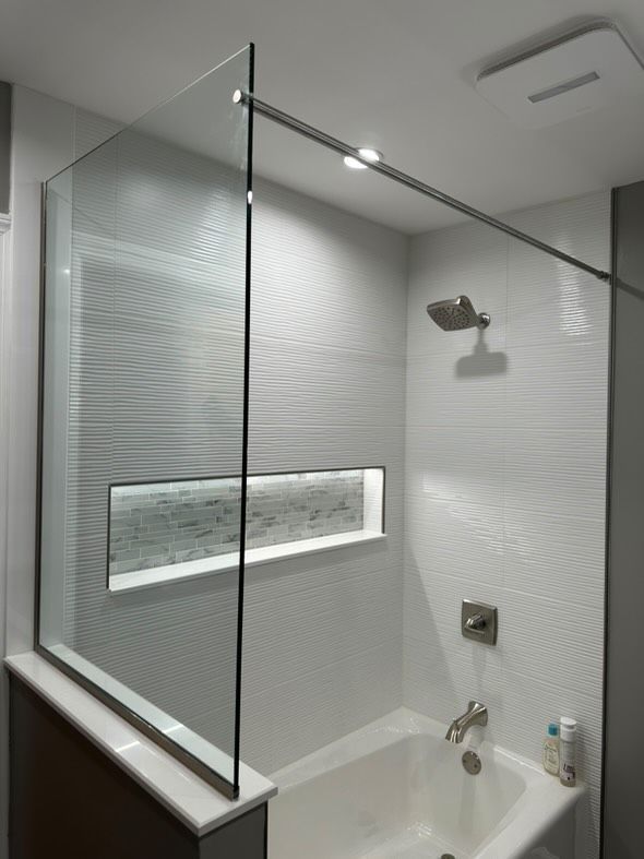 Modern bathroom with glass shower enclosure, white tile walls, built-in shelf, and bathtub faucet.