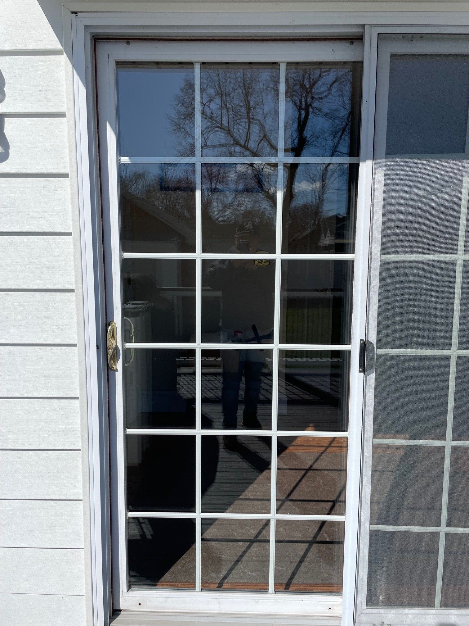 White patio door with glass panes and reflections, next to a window on a light siding exterior.