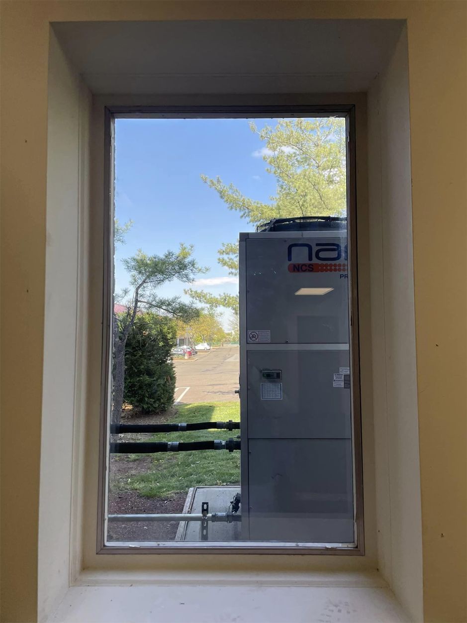 View through a window of a gray utility unit outside with trees and blue sky in the background